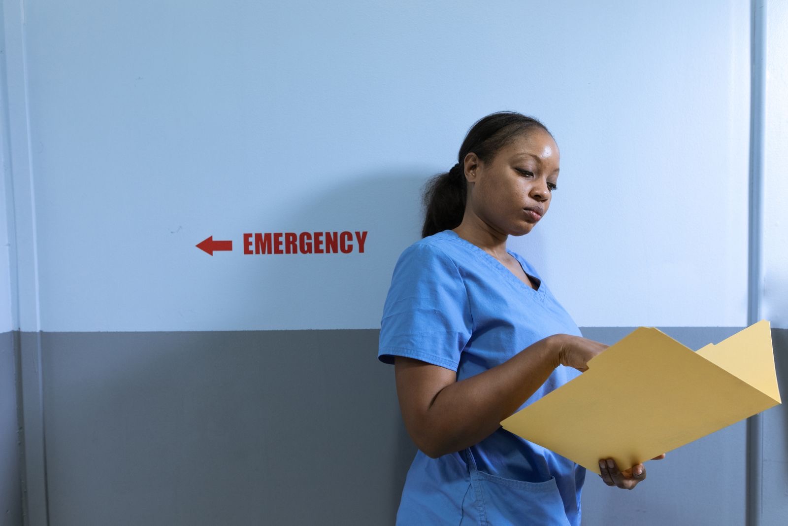 Nurse in scrubs reading a chart in a hospital corridor